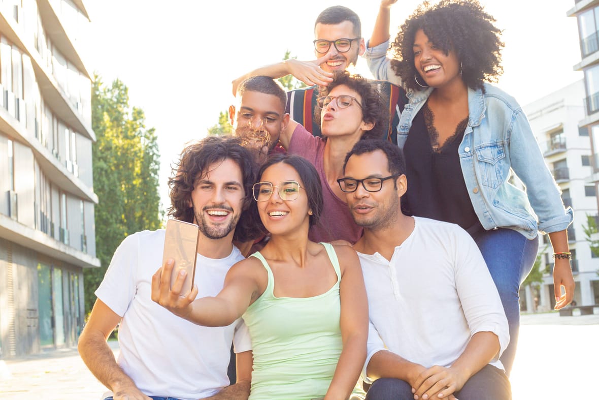 Joyous mix raced people taking group selfie outdoors. Interracial team of friends posing, grimacing, gesturing and smiling at phone camera. Photo concept