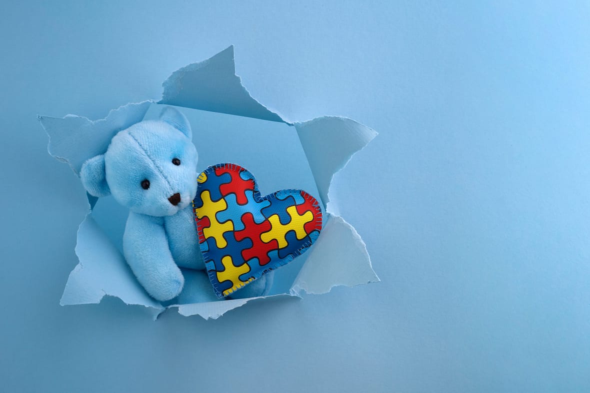 World Autism Awareness, concept with teddy bear holding puzzle or jigsaw pattern on heart in blue paper cut hole