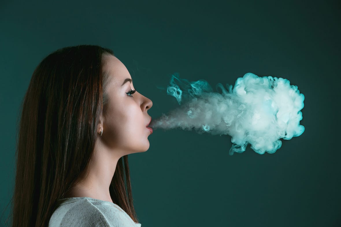 The face of vaping young woman on black studio background