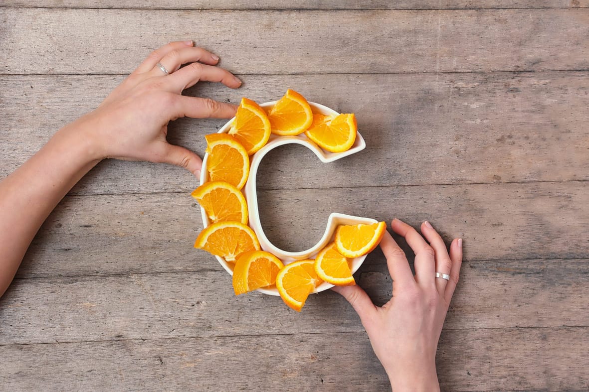 Vitamin C nutrient in food concept. Woman hands holding plate in shape of letter C with orange slices on wooden background. Flat lay or top view. Ascorbic acid is important for immune system function.